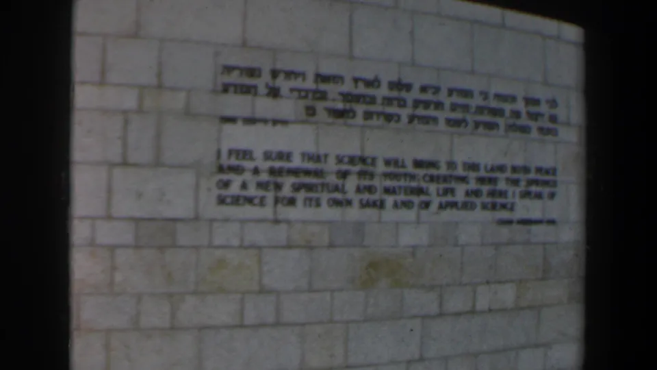 1960 Israel 8mm frame showing Hebrew and English text painted or mounted on a pale stone block wall.