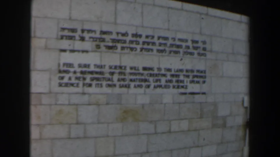 1960 Israel 8mm still with the bilingual inscription slightly lower in frame and dark contact-sheet borders visible.