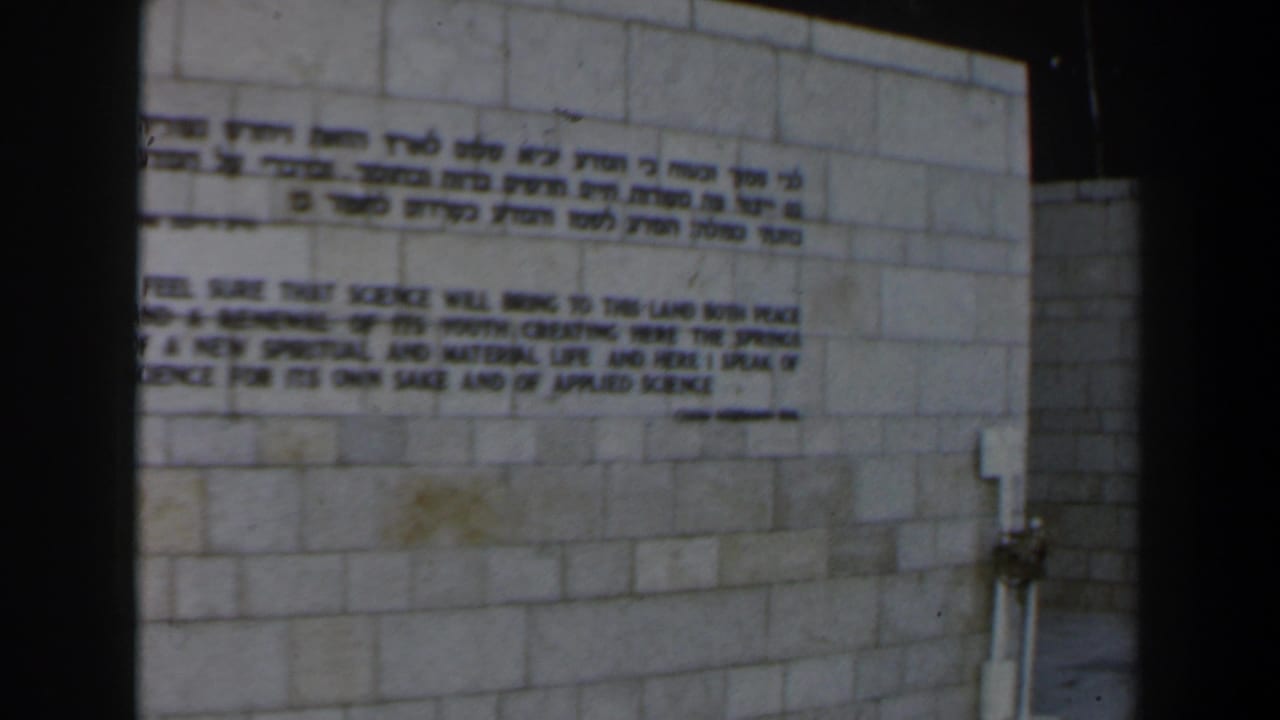Stone wall with Hebrew and English text, seen in soft 8mm color.