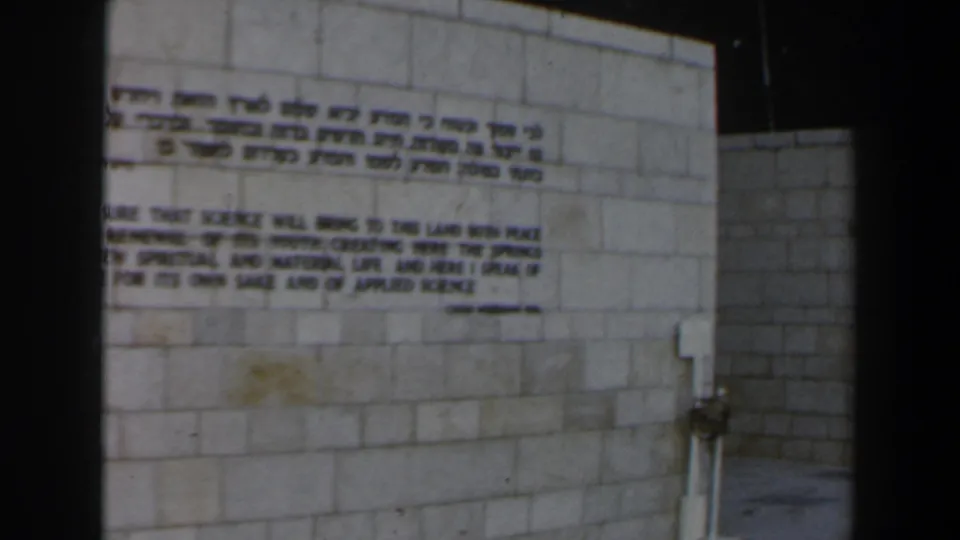 1960s Israel frame holding on a bilingual inscription across a pale stone-block wall.