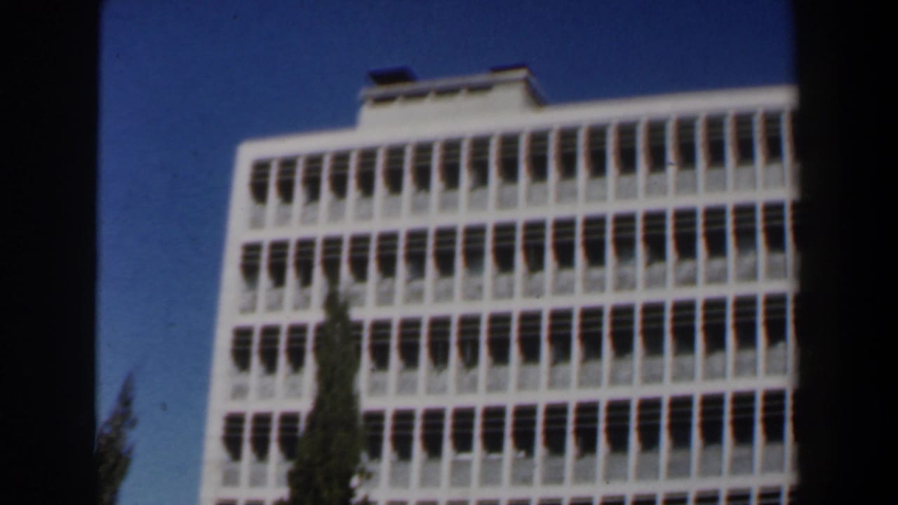 1960 Israel 8mm frame showing a white modernist building with rows of windows viewed from below.