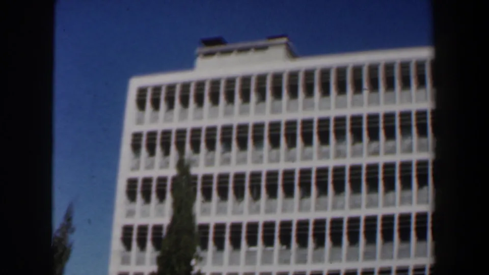 1960 Israel 8mm frame showing a white modernist building with rows of windows viewed from below.