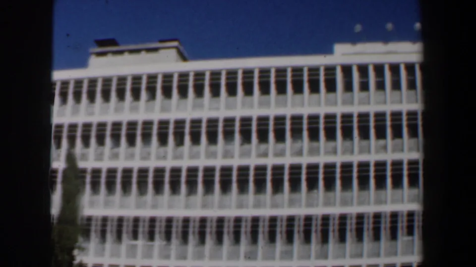 White multi-story building in Israel, 1960, framed with dark 8mm borders and deep blue sky.