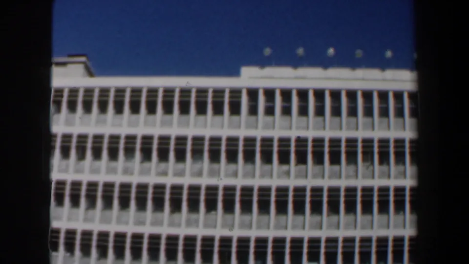 Low-angle 8mm view of a white Israeli building facade, showing repeated windows and rooftop fixtures.