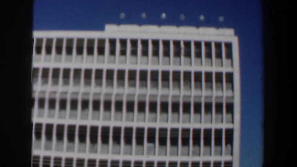 Final 1960 Israel frame of a white multi-story building, with soft 8mm focus and dark edge borders.