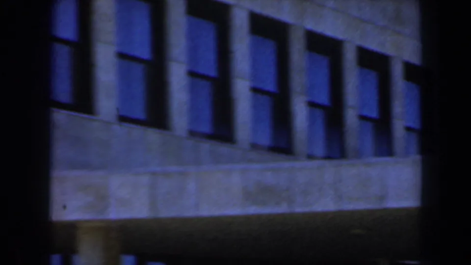 A dark blue-tinted 8mm frame shows the same or similar modern building facade at night or under low exposure, with rows of rectangular windows.