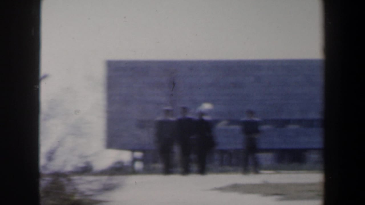 Blurred view of people near a low building and large shaded wall area.