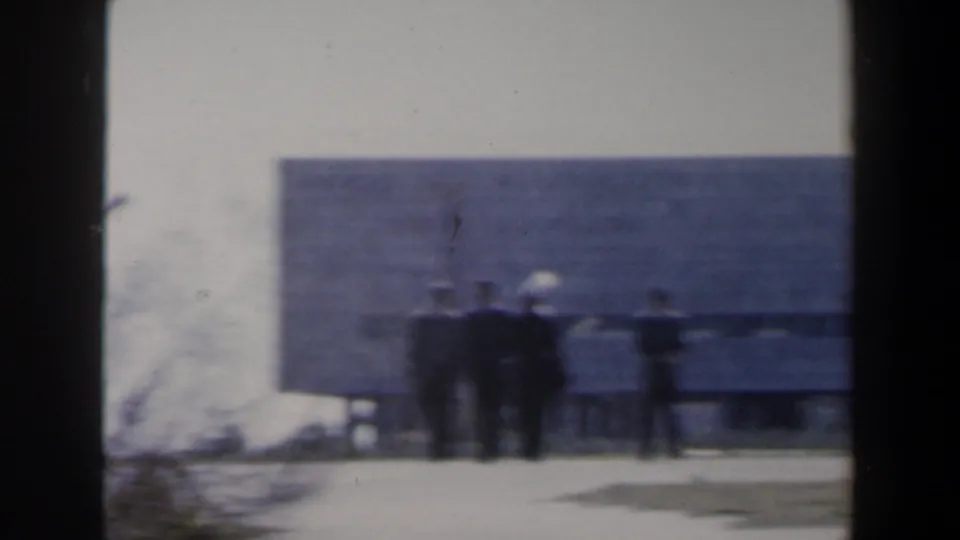 Soft 8mm frame from Israel around 1960 showing people near a low modern building in bright daylight.