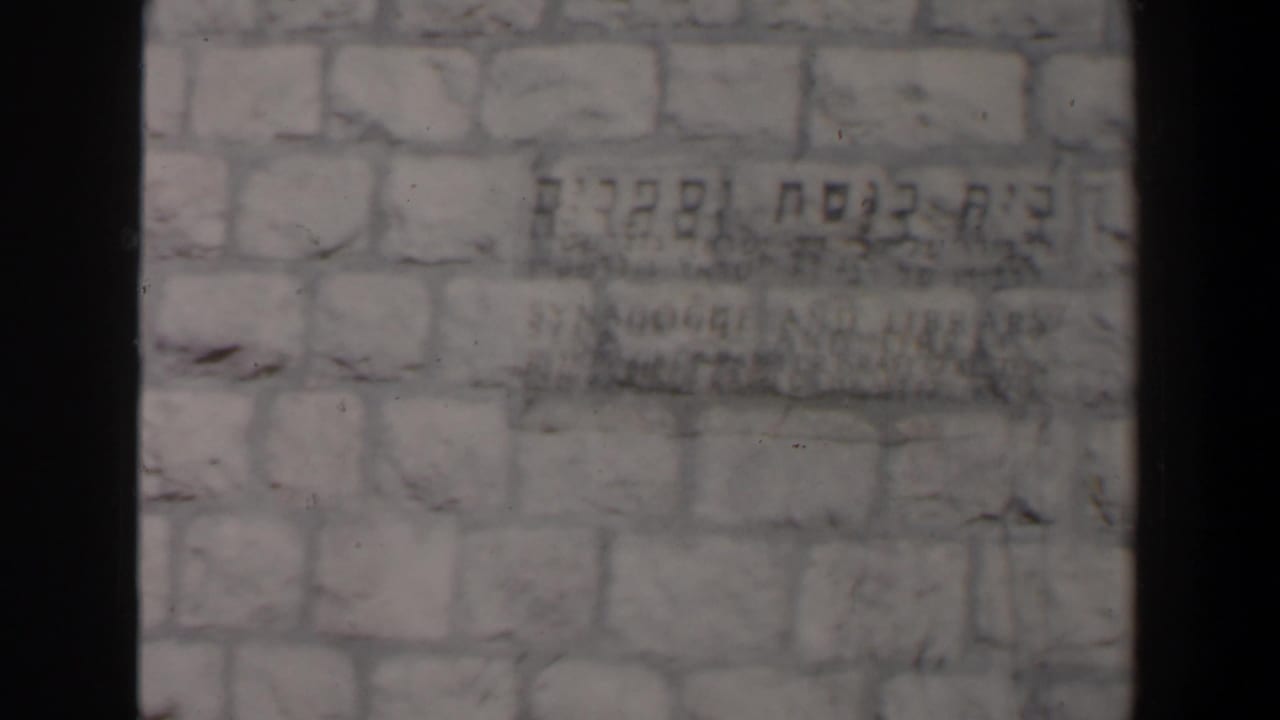 Close view of a pale stone wall with Hebrew lettering and dark film edge shadows.