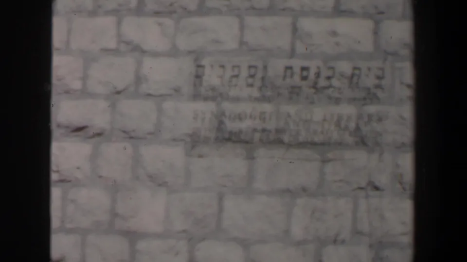 Close-up of a weathered stone wall in Israel with Hebrew text visible but not clearly readable in the soft 8mm frame.