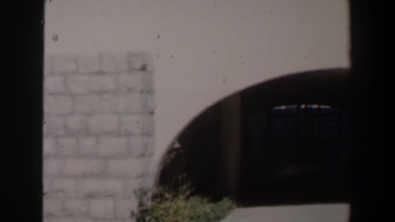 Pale stone wall and dark arched entrance seen from a sunlit walkway.