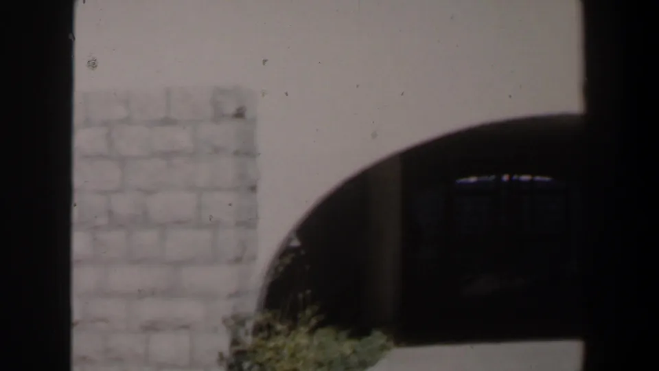 1960s Israel 8mm frame showing pale stonework, a shadowed archway, dark gates and low plants near the path.