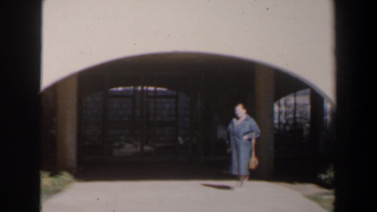 Woman in a blue dress walks near a large arched entrance carrying a small basket.