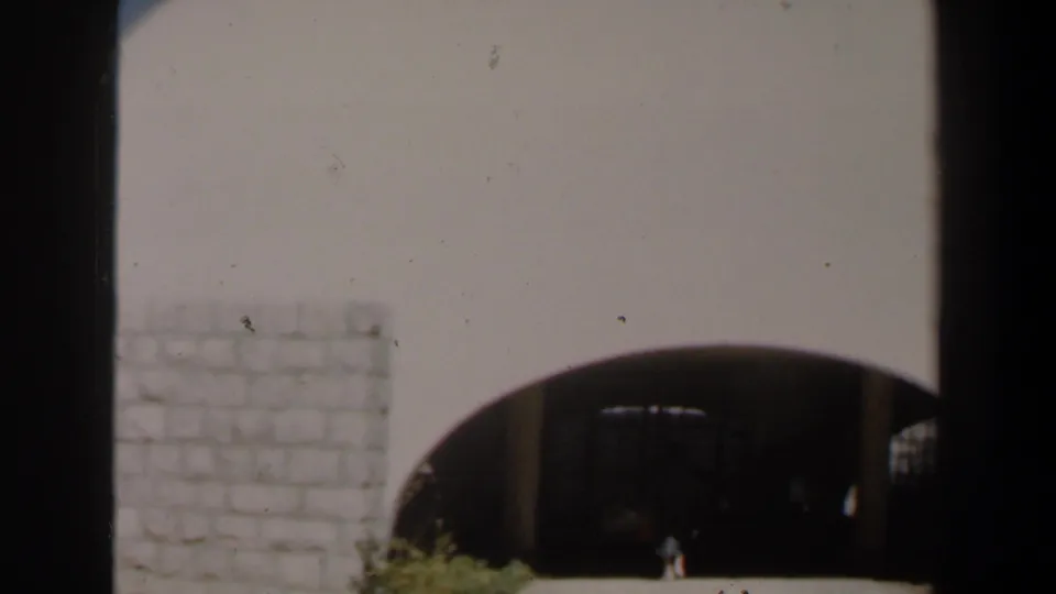Final 8mm frame shows the pale wall and arched entrance after the woman has nearly passed into the dark interior.