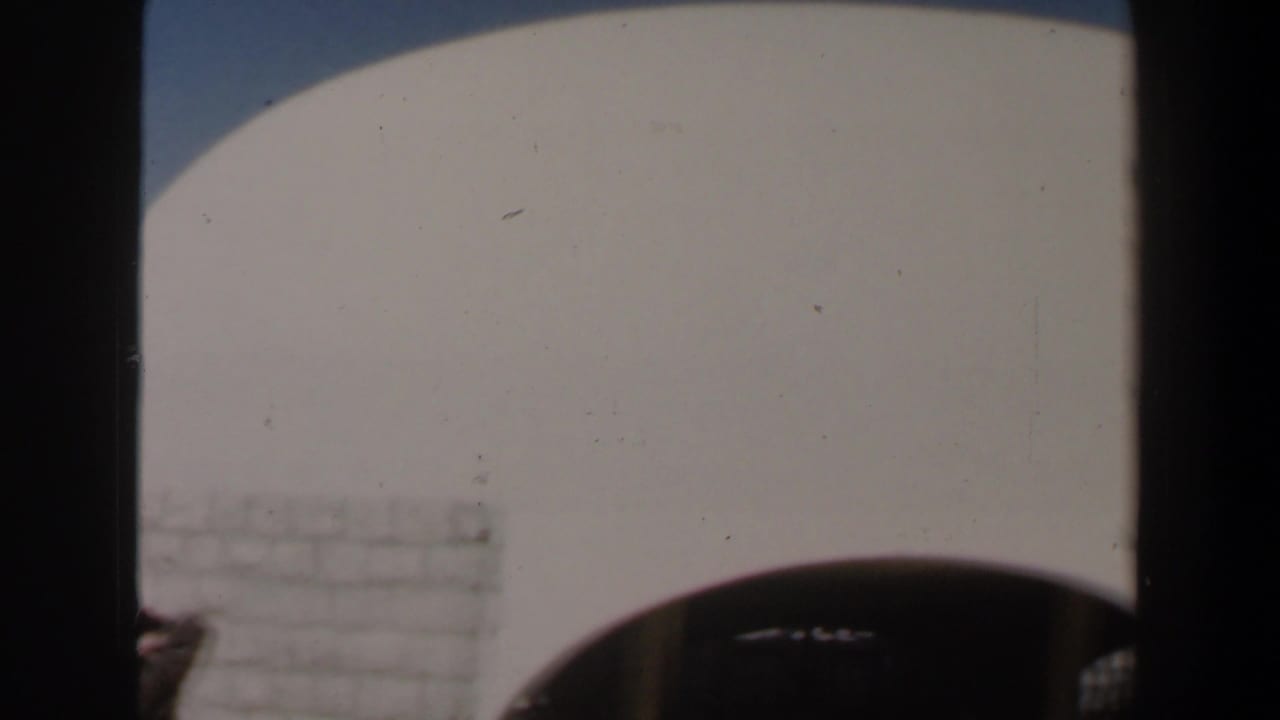 1960 Israel 8mm frame showing a pale arched exterior wall, dark foreground posts, and bright blue sky.