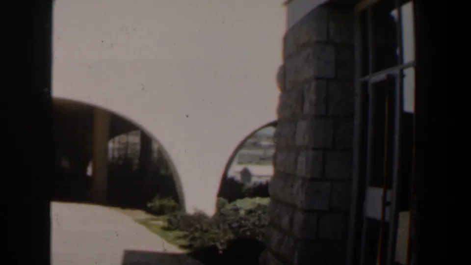 1960 Israel 8mm frame looking toward a shaded arched porch, stone wall, walkway, and low garden planting.
