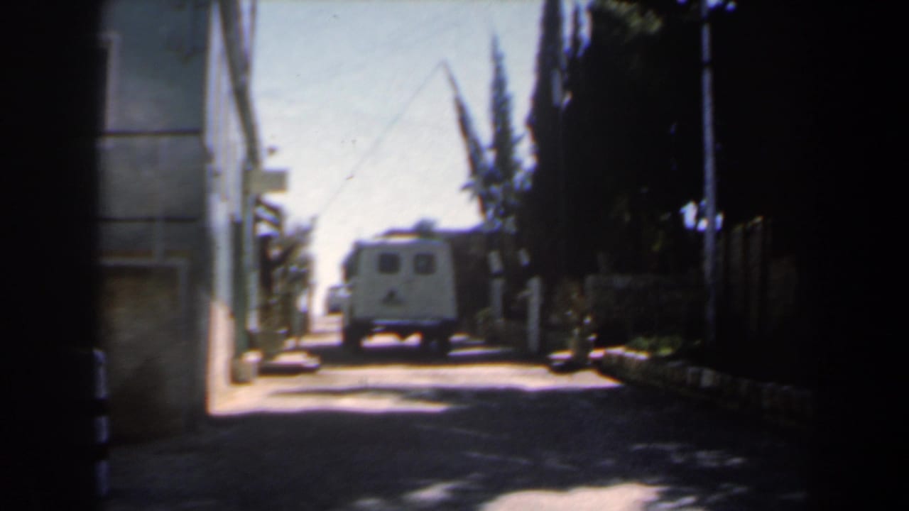 1960s Israel street view with a white van in bright distance, a pale building edge on the left, dark foliage on the right, and high-contrast shade in the foreground.