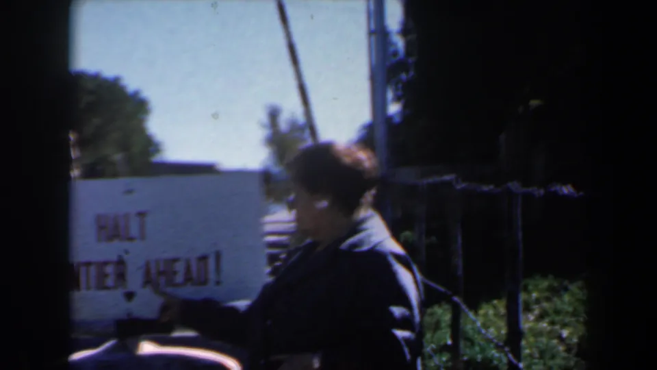 A person in dark clothing points near a white HALT FRONTIER AHEAD sign in a 1960 Israel home-movie frame.