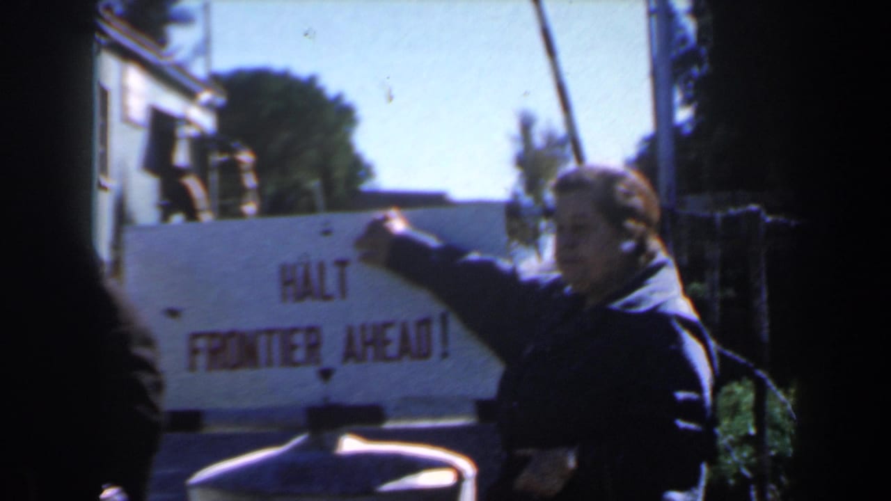 Woman in a dark coat points at a white sign reading HALT FRONTIER AHEAD.