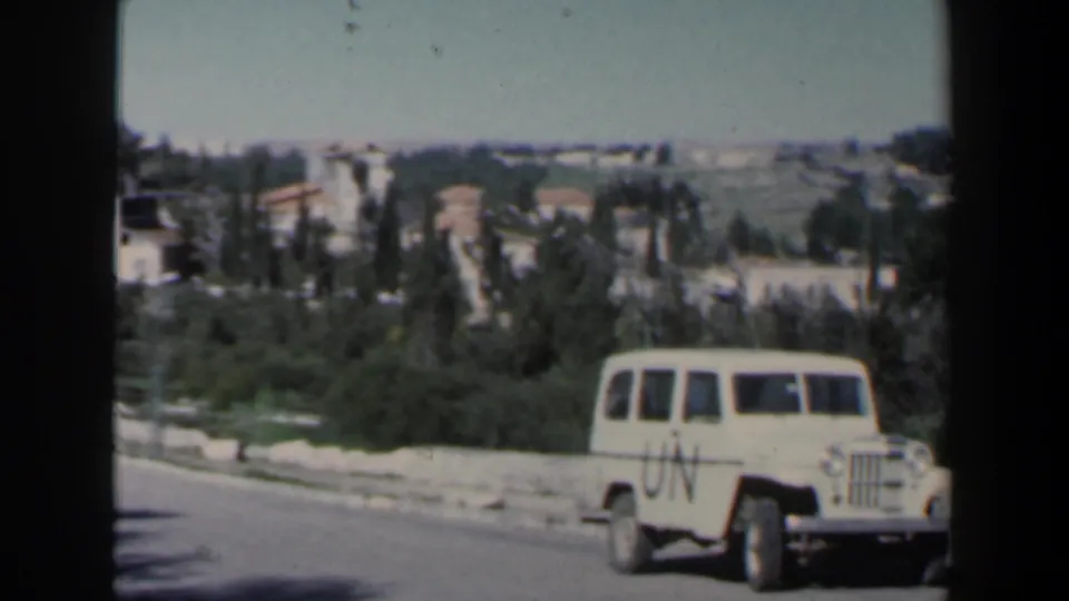 The UN-marked Jeep continues along the paved road in Israel, framed by roadside greenery and low hillside structures.