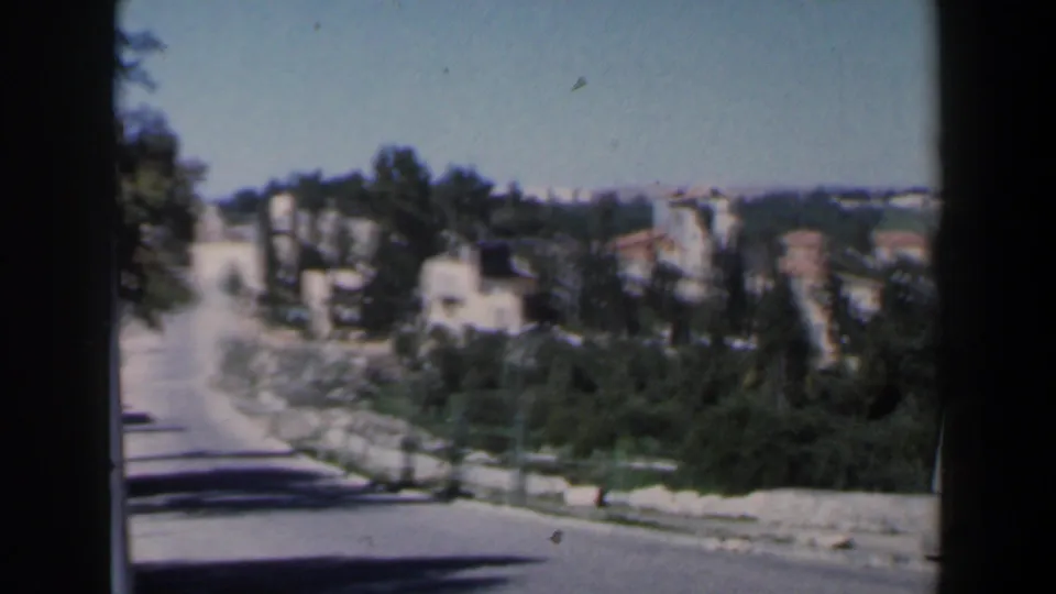 A wider roadside view shows the curving road, trees and hillside buildings, with the UN-marked vehicle no longer prominent in frame.