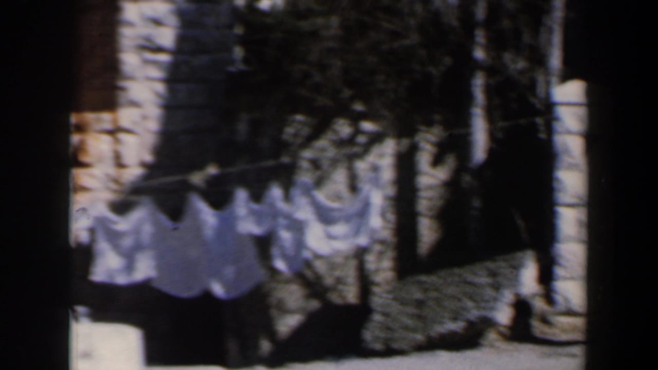 Close home-movie view of laundry hanging near a pale stone wall, with strong shadowing and cropped framing.