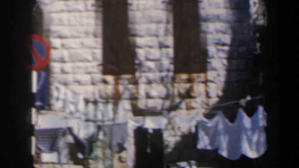 1960 Israel street detail showing a stone building facade with closed shutters, laundry on a line, and a no-parking sign at the edge.