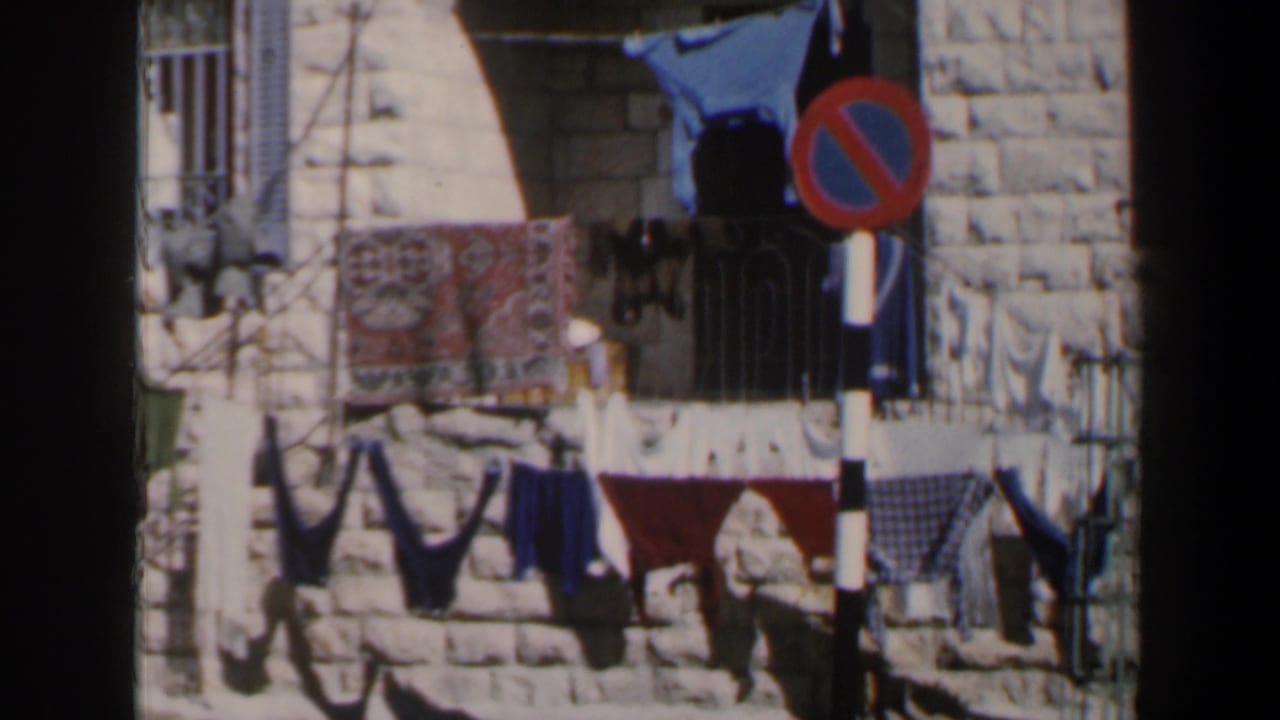 Stone building with hanging laundry and a red-blue no-parking sign in front.