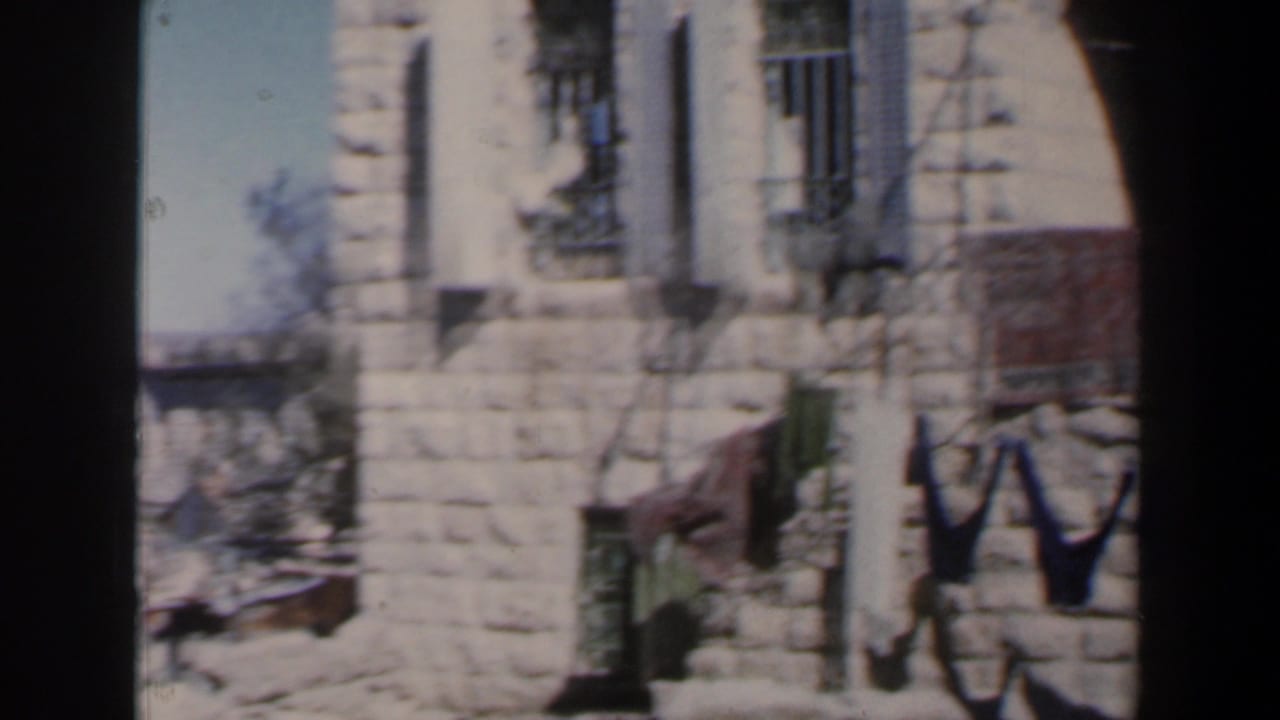 Soft 8mm frame from Israel showing a stone exterior, barred windows, shadows, and partial laundry at the side.