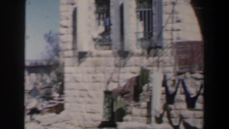 Soft 8mm frame from Israel showing a stone exterior, barred windows, shadows, and partial laundry at the side.