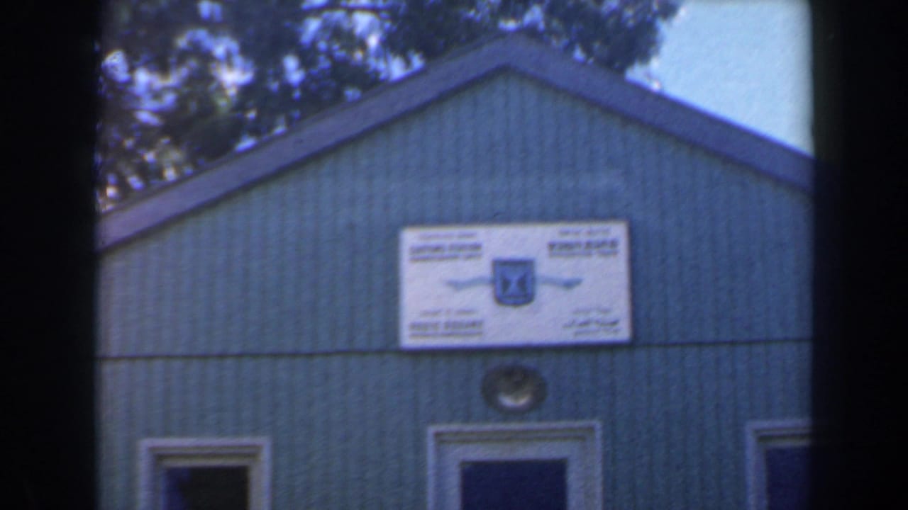 1960 Israel 8mm frame showing a green-sided gabled building with a white sign and blue emblem mounted above the doorway.