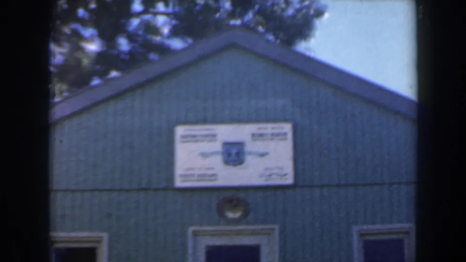 1960 Israel 8mm frame with the signed green building centered under trees, showing soft focus and visible film gate edges.