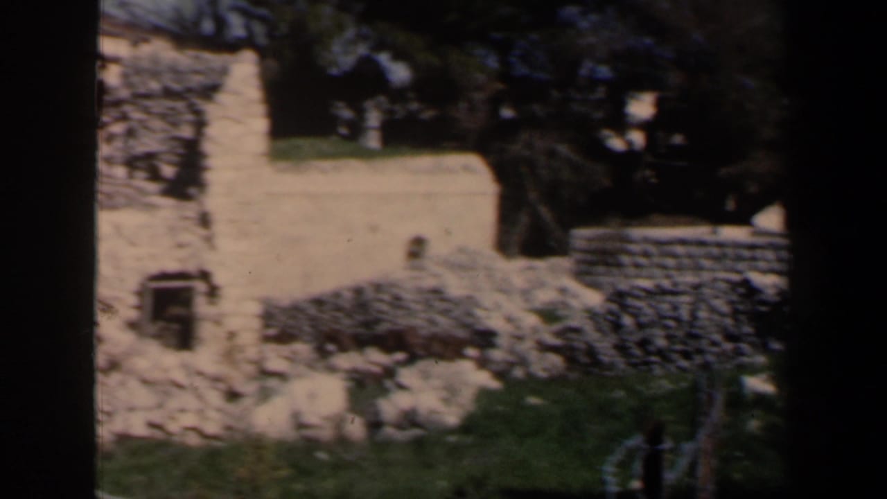 Stone walls and grassy ground seen through a dark film-frame edge.
