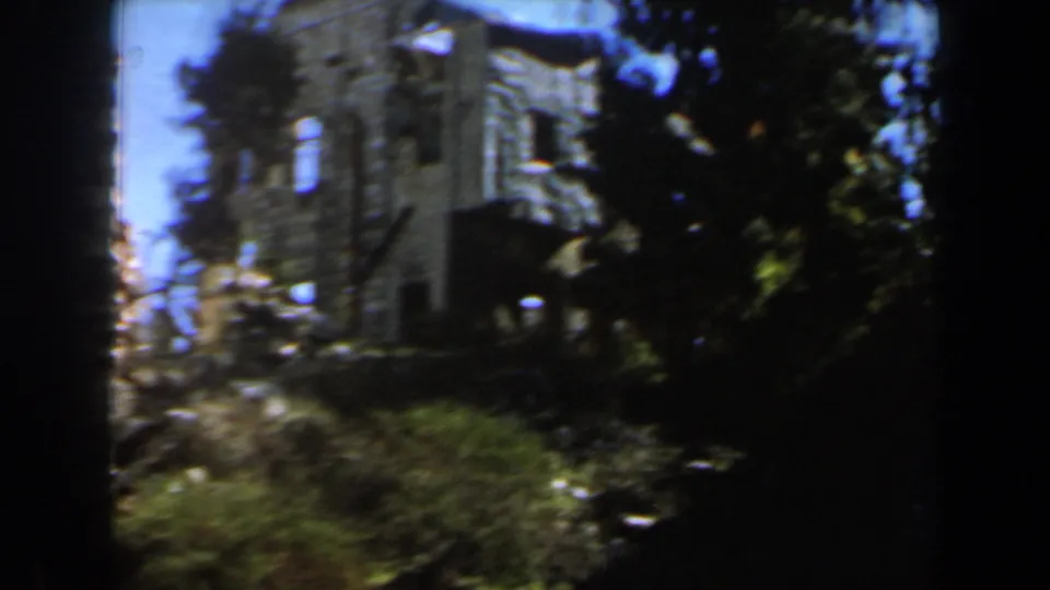 1960s Israel 8mm frame with a closer visitor view of broken grey stone walls, window openings, trees, and low shrubs.
