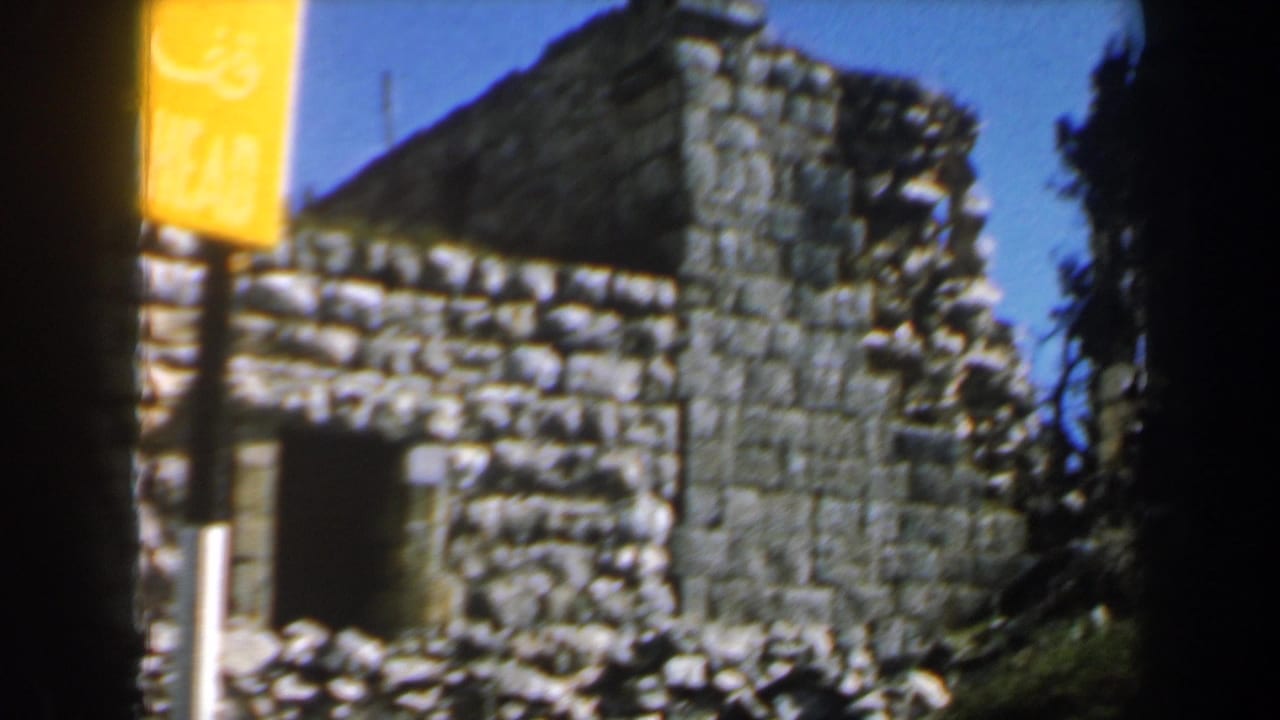Weathered stone structure with a dark doorway, grass, and a yellow signpost.