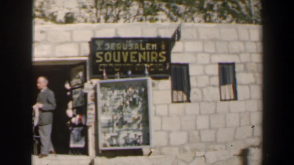 1960 Israel 8mm frame showing a man outside a souvenir shop entrance with a Jerusalem Souvenirs sign in English and Hebrew.
