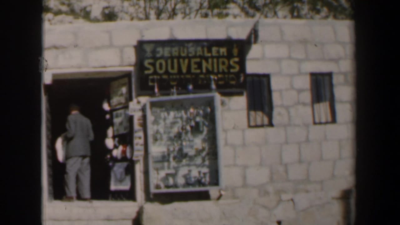 A suited man faces the doorway of a souvenir shop under a Jerusalem Souvenirs sign.