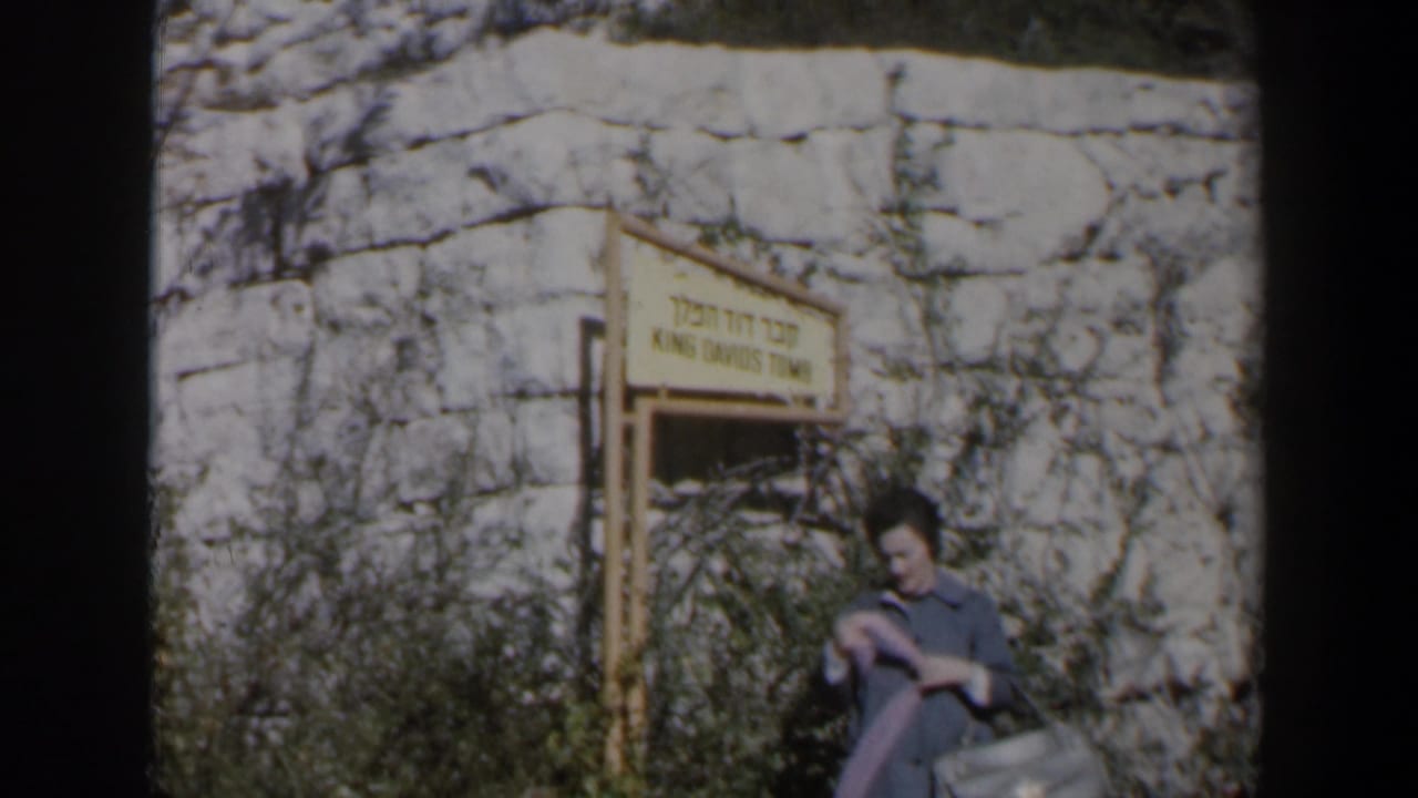 Woman adjusting a pink garment near the King David's Tomb entrance sign.