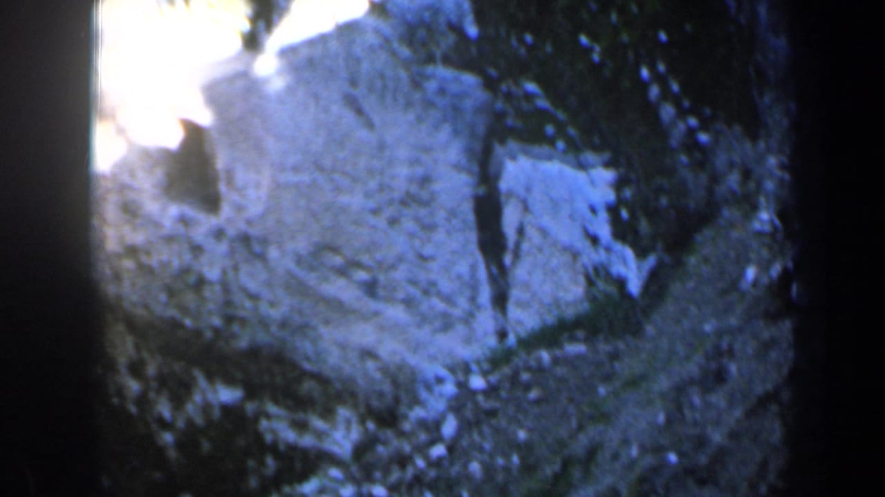 1960 Israel 8mm frame showing a pale rocky cliffside from above, with tree shadows, soft focus, and blue-tinted exposure.