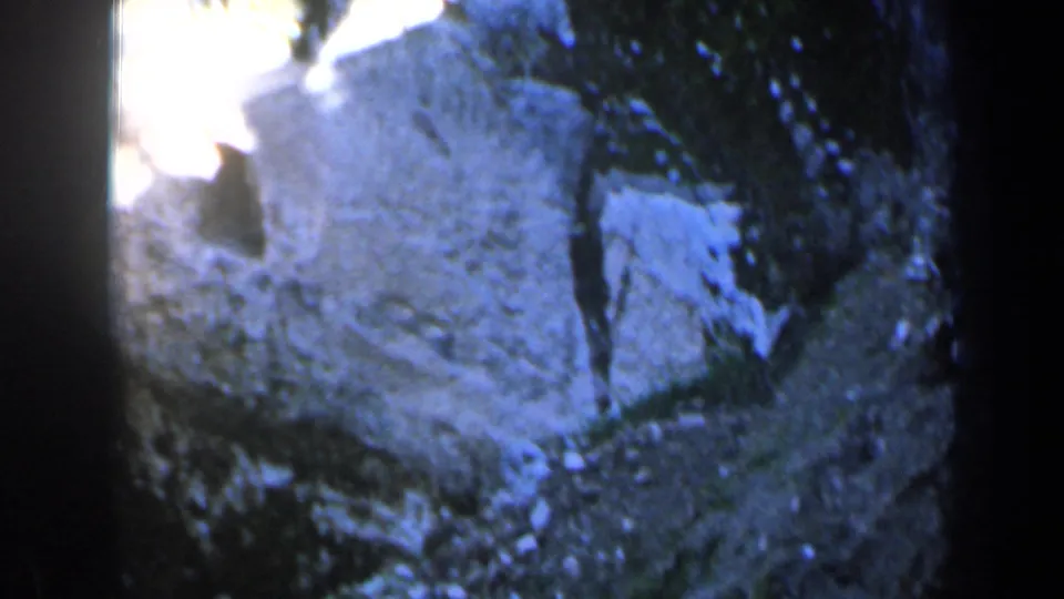 1960 Israel 8mm frame showing a pale rocky cliffside from above, with tree shadows, soft focus, and blue-tinted exposure.