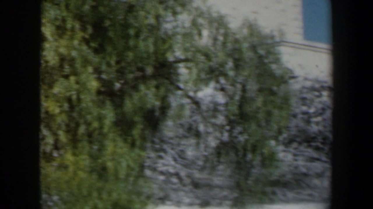 White stone wall and greenery beside a church tower, partly obscured by dark film edges.