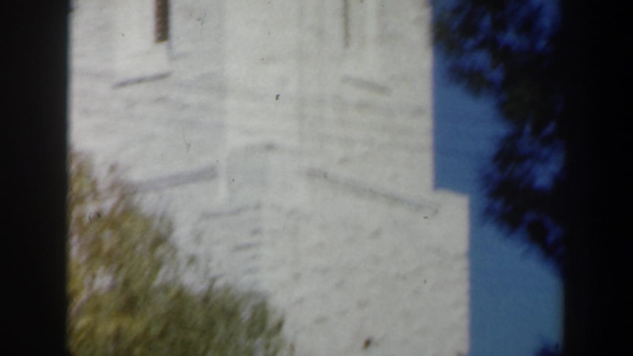 Pale stone church tower detail in Israel, filmed in soft 1960s 8mm color with blue sky at the edge.