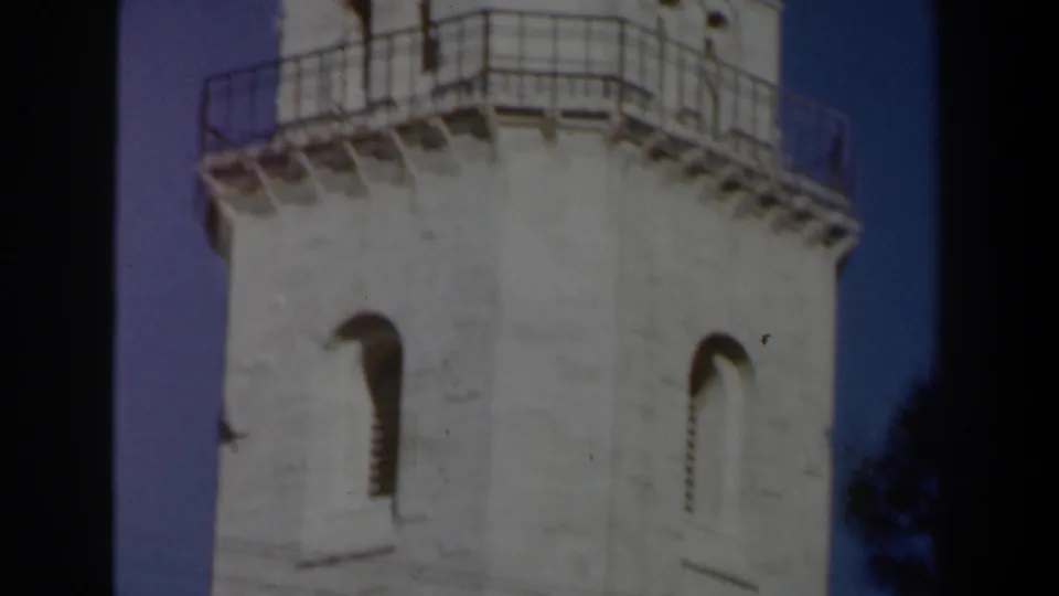 1960s Israel frame showing the upper church tower with arched windows and a metal balcony railing against blue sky.
