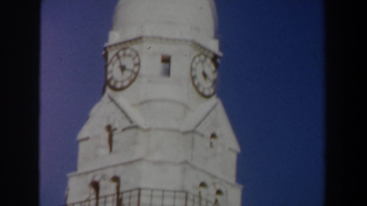 Upper section of a pale stone clock tower against a deep blue sky.