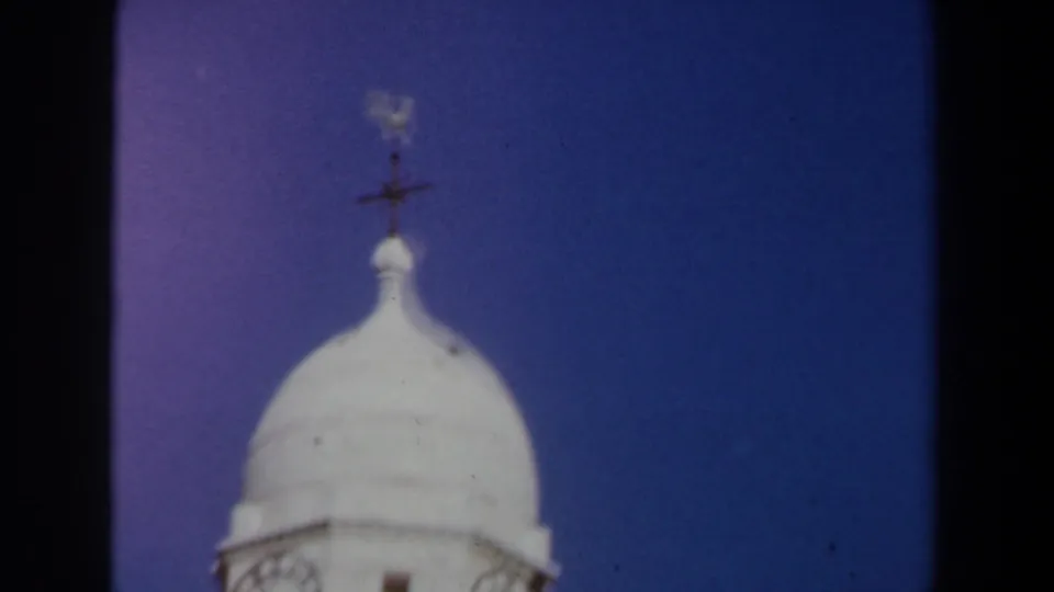 1960 Israel 8mm frame showing the domed top of a pale stone tower, balcony railing, and weather vane against blue sky.