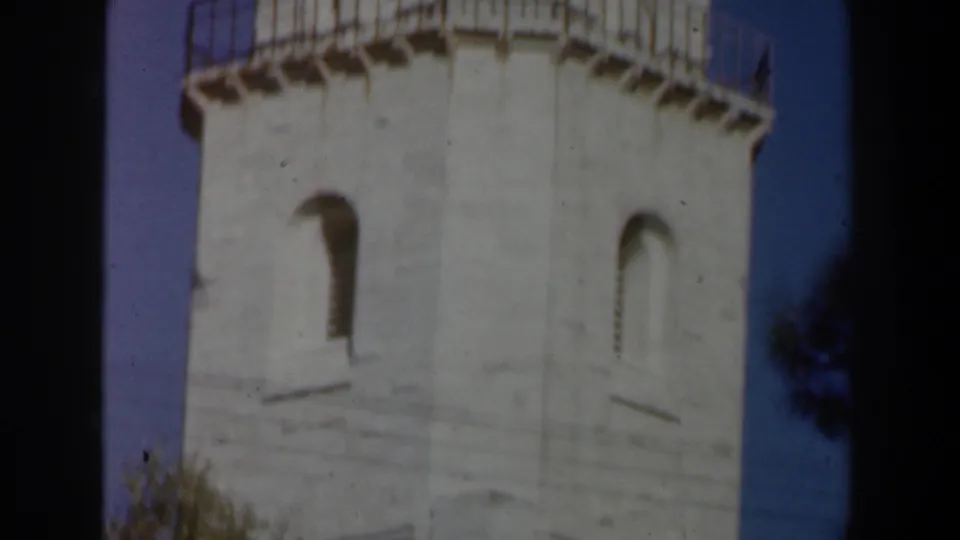 1960 Israel 8mm frame showing the tower body with arched windows, upper railing, dome, and a small patch of foliage at the edge.