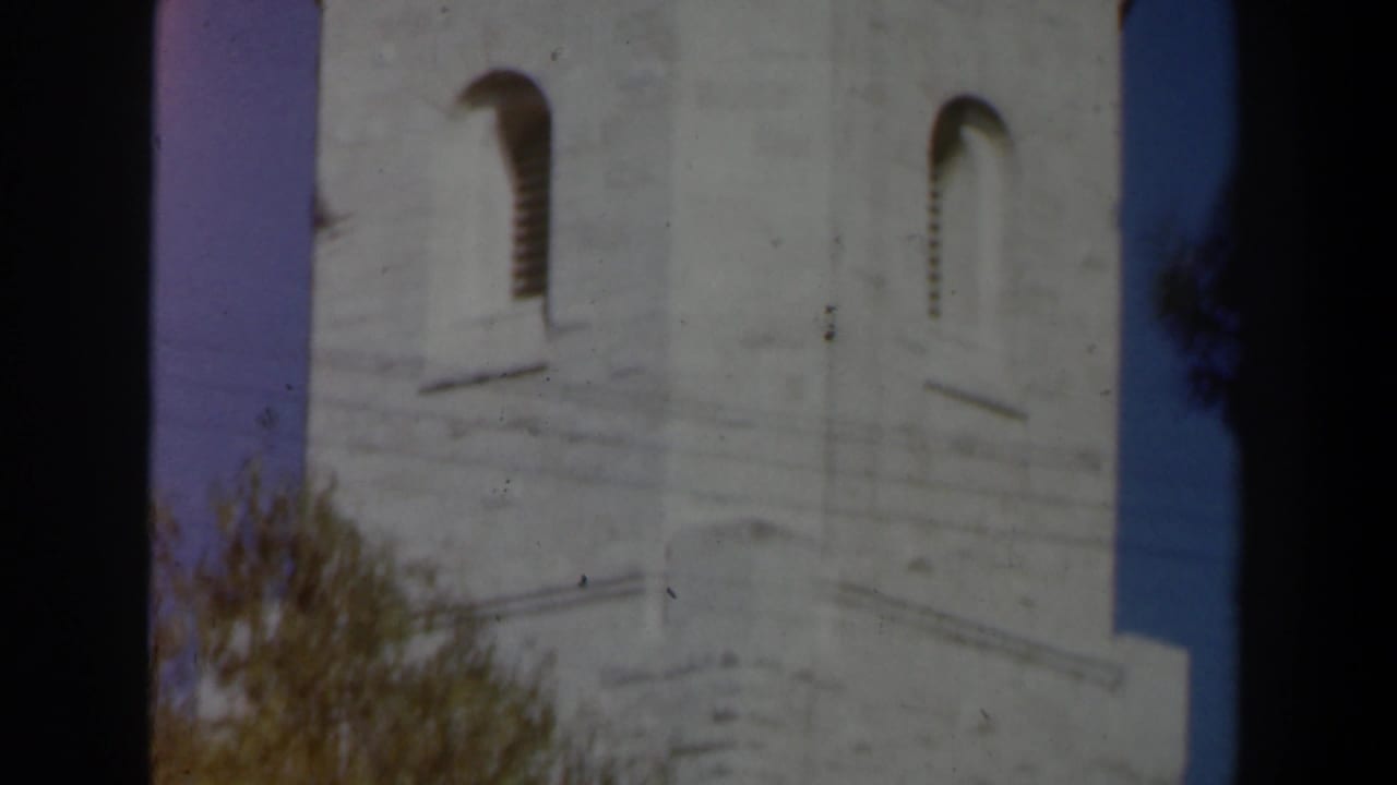 1960 Israel 8mm frame showing a pale stone tower with arched openings, partly framed by trees and dark film edges.