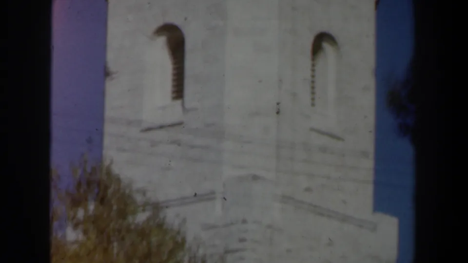 1960 Israel 8mm frame showing a pale stone tower with arched openings, partly framed by trees and dark film edges.