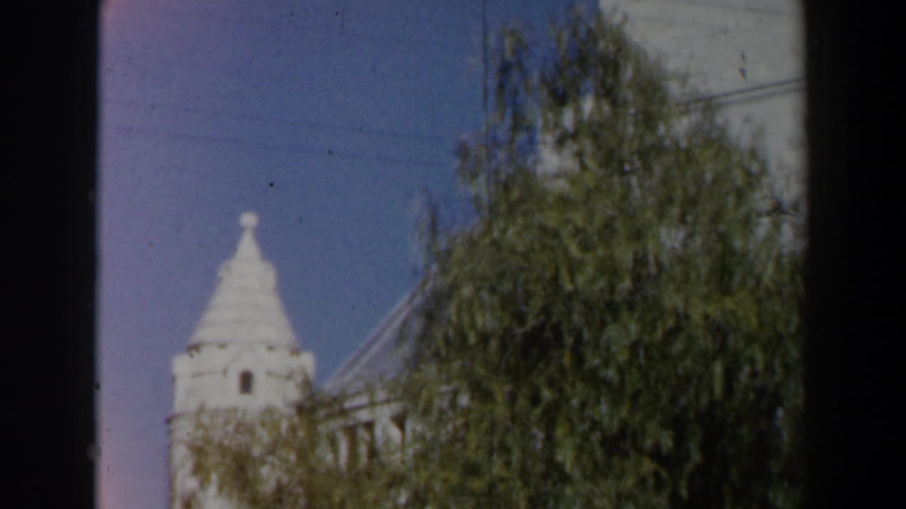 1960 Israel home-movie frame with a white conical-roof tower partly obscured by green foliage and film gate edges.