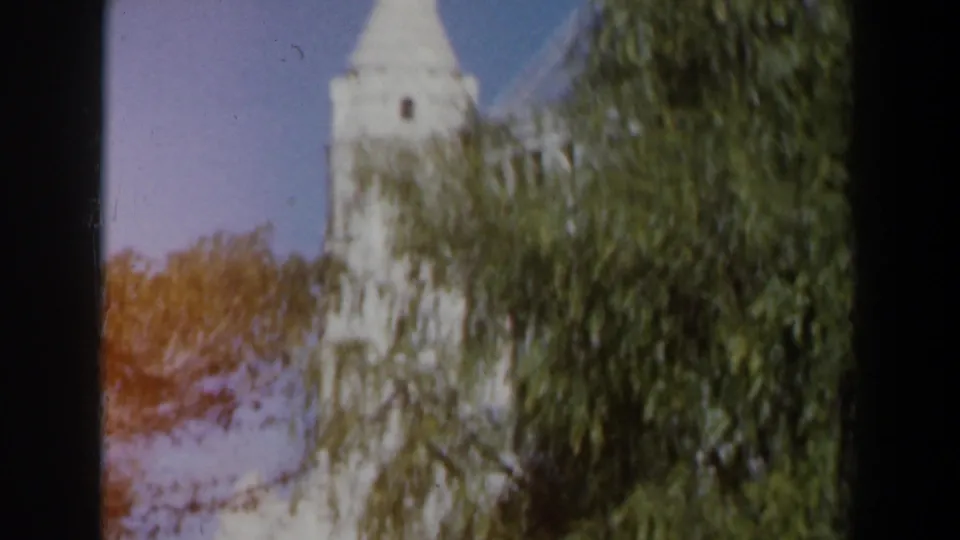 1960 Israel 8mm view of a white tower partly covered by leafy trees, with blue sky and visible color fading.